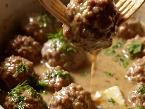 A close-up of tender cocktail meatballs coated in a rich, velvety ivory cream gravy inside a ceramic slow cooker.
