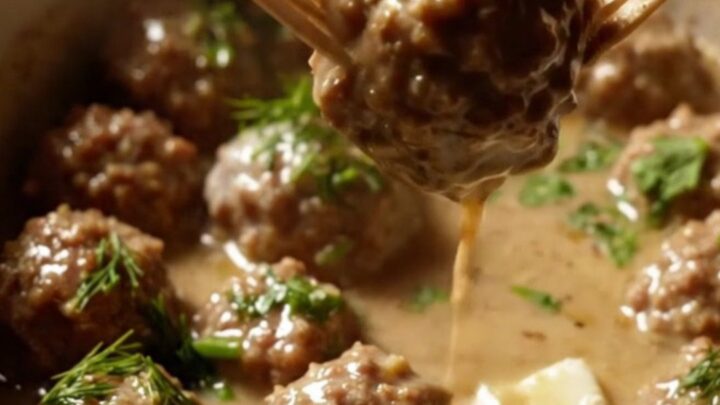 A close-up of tender cocktail meatballs coated in a rich, velvety ivory cream gravy inside a ceramic slow cooker.