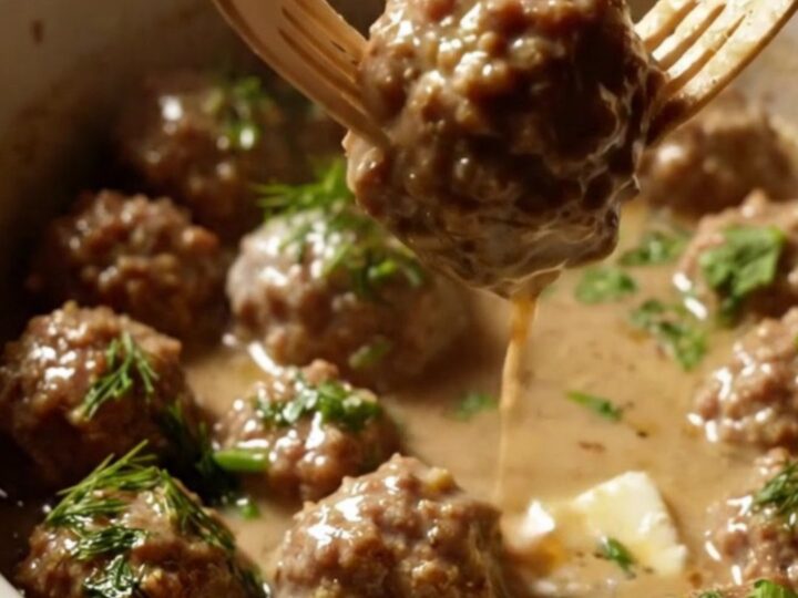 A close-up of tender cocktail meatballs coated in a rich, velvety ivory cream gravy inside a ceramic slow cooker.