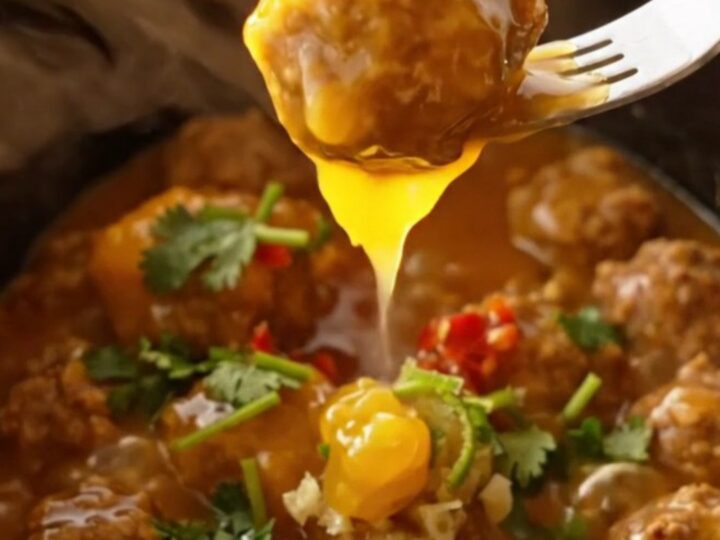 A close-up shot of glossy, golden-orange glazed chicken meatballs in a ceramic slow cooker.