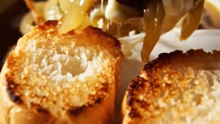 A close-up of tender beef meatballs in a ceramic slow cooker, topped with melted, gooey Gruyere cheese and fresh thyme.