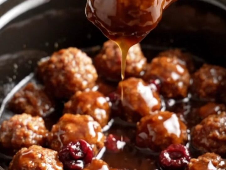 A close-up of glossy, dark mahogany-glazed meatballs in a cherry-red ceramic slow cooker.