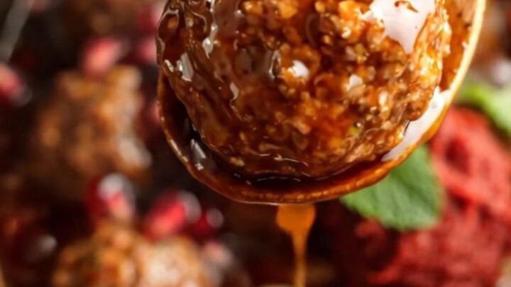 A close-up of pomegranate and harissa glazed lamb meatballs in a terracotta crockpot, garnished with fresh mint and arils.