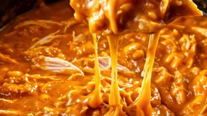 A close-up of a pita chip being dipped into a creamy, bubbling honey sriracha chicken dip in a black crockpot.