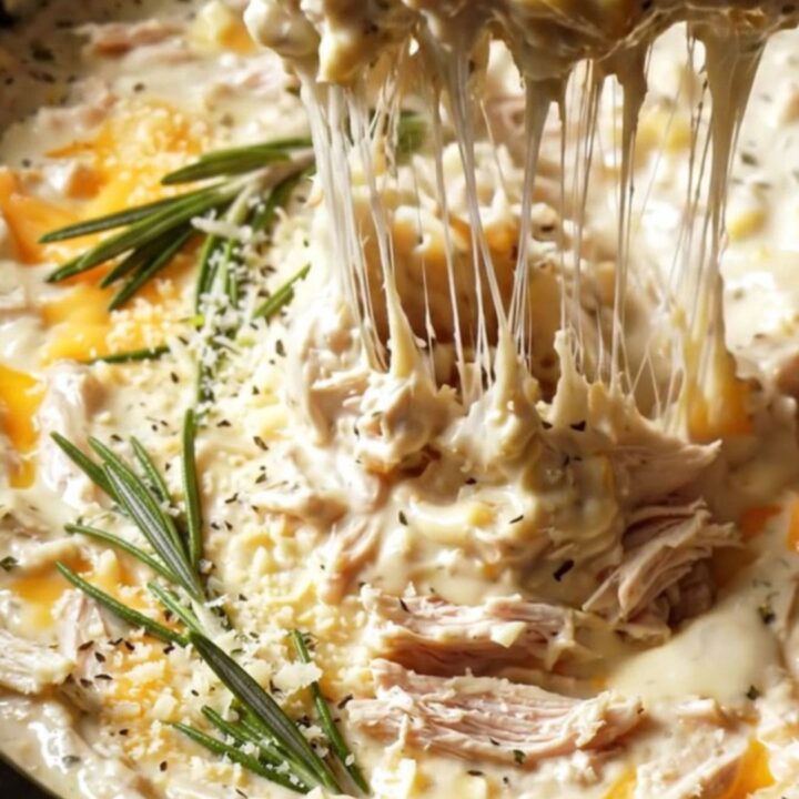 A close-up of a creamy garlic Parmesan buffalo chicken dip in a ceramic crockpot with a cheese pull.