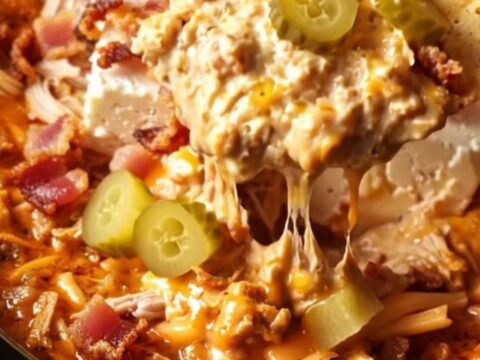 A cinematic close-up of a chip being dipped into a creamy, fiery red chicken dip inside a red ceramic slow cooker.