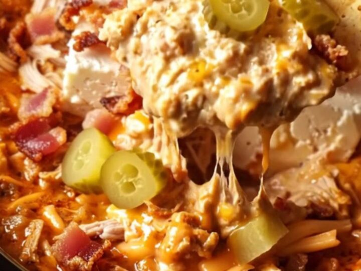 A cinematic close-up of a chip being dipped into a creamy, fiery red chicken dip inside a red ceramic slow cooker.