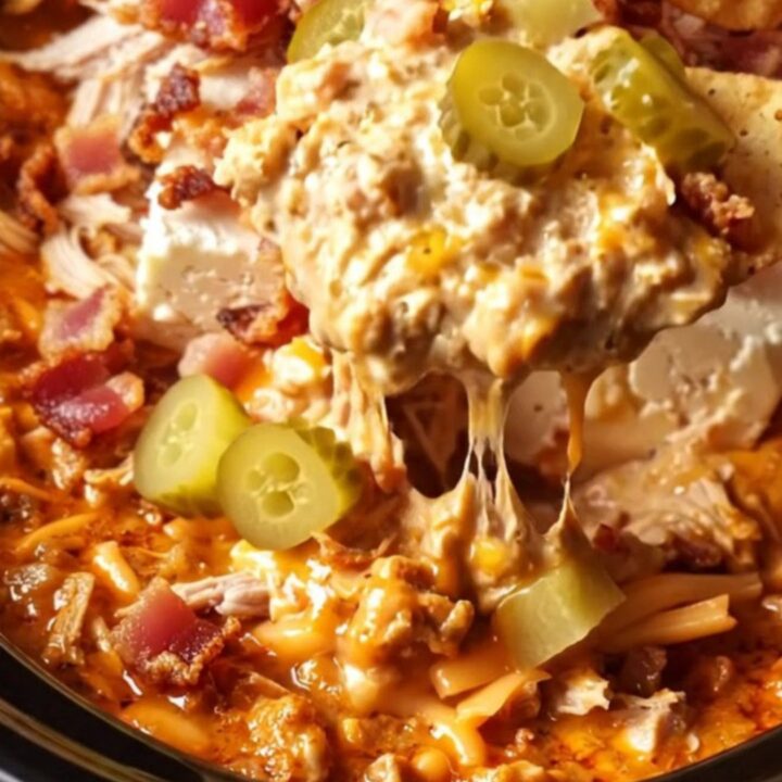 A cinematic close-up of a chip being dipped into a creamy, fiery red chicken dip inside a red ceramic slow cooker.