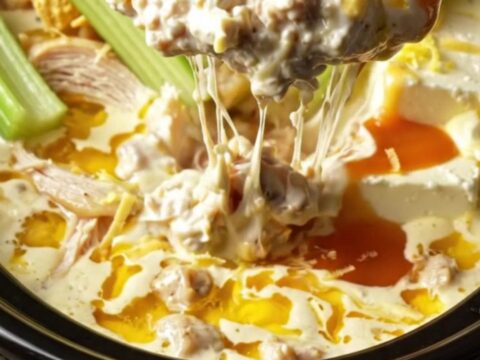 A warm ceramic slow cooker filled with creamy, bubbling lemon pepper chicken dip, garnished with fresh charred lemon slices.