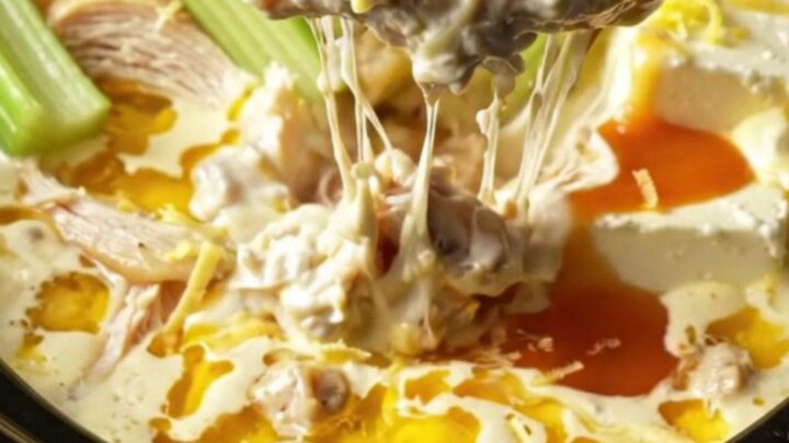 A warm ceramic slow cooker filled with creamy, bubbling lemon pepper chicken dip, garnished with fresh charred lemon slices.