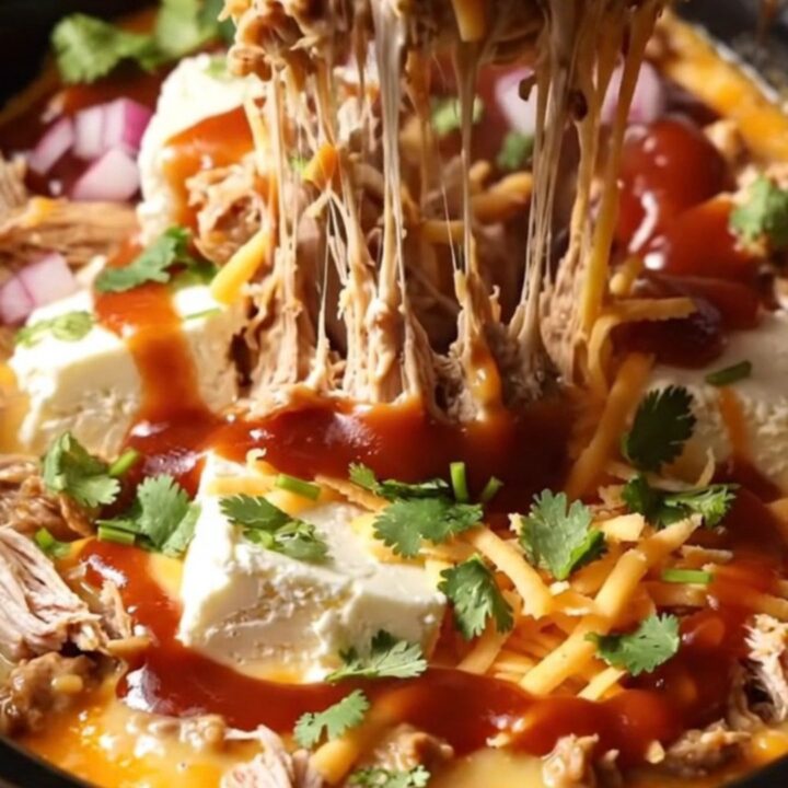A dark bronze ceramic slow cooker filled with creamy BBQ pulled chicken dip topped with cilantro.