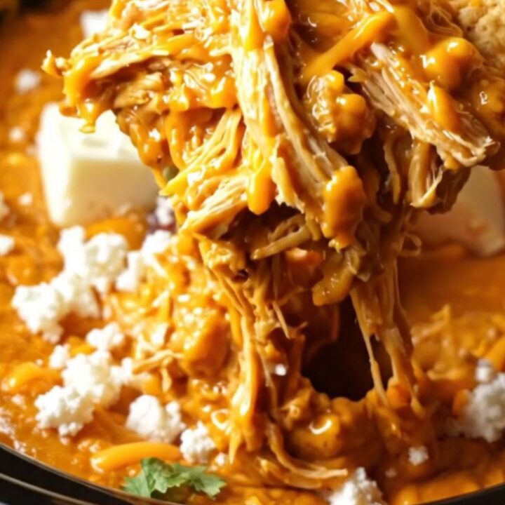 A warm ceramic slow cooker filled with creamy chipotle honey lime chicken dip topped with cotija cheese and cilantro.