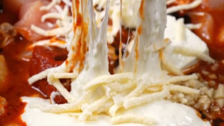 A close-up of a spicy Korean chicken dip in a black ceramic pot with a massive mozzarella cheese pull.