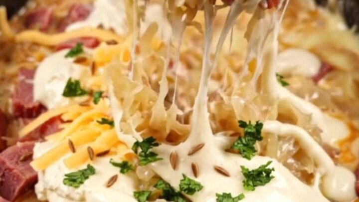A close-up of a bubbling, creamy Reuben dip in a dark stoneware crockpot with a piece of toasted marbled rye bread.