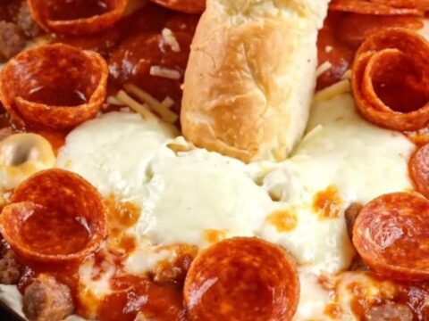 A bright red slow cooker filled with bubbling, cheesy pizza dip topped with crispy pepperoni and fresh basil.