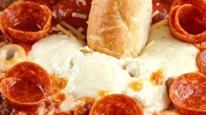 A bright red slow cooker filled with bubbling, cheesy pizza dip topped with crispy pepperoni and fresh basil.