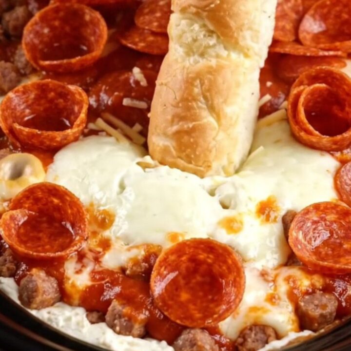 A bright red slow cooker filled with bubbling, cheesy pizza dip topped with crispy pepperoni and fresh basil.