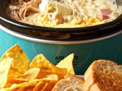 A close-up of a warm, creamy Cuban sandwich dip in a turquoise ceramic crockpot, scooped with a crispy plantain chip.