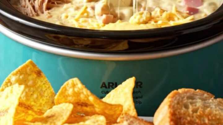 A close-up of a warm, creamy Cuban sandwich dip in a turquoise ceramic crockpot, scooped with a crispy plantain chip.