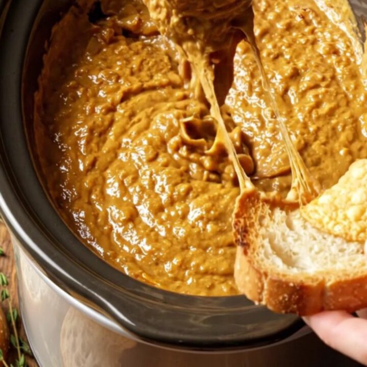 A close-up shot of a toasted baguette dipped into a bubbling, golden-brown French onion and Gruyere dip.
