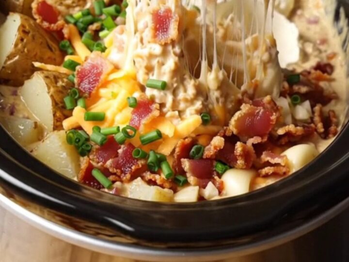 A creamy, molten baked potato dip in a black Crockpot, topped with fresh chives and crispy bacon.