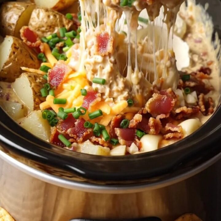 A creamy, molten baked potato dip in a black Crockpot, topped with fresh chives and crispy bacon.