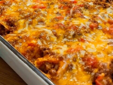 A slice of golden-brown beef enchilada casserole being lifted from a white ceramic baking dish