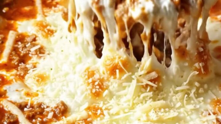 A warm, bubbling lasagna dip in a deep red crockpot, with a piece of garlic bread pulling away a long string of melted