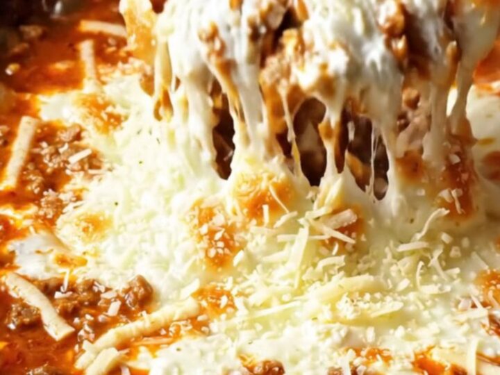 A warm, bubbling lasagna dip in a deep red crockpot, with a piece of garlic bread pulling away a long string of melted