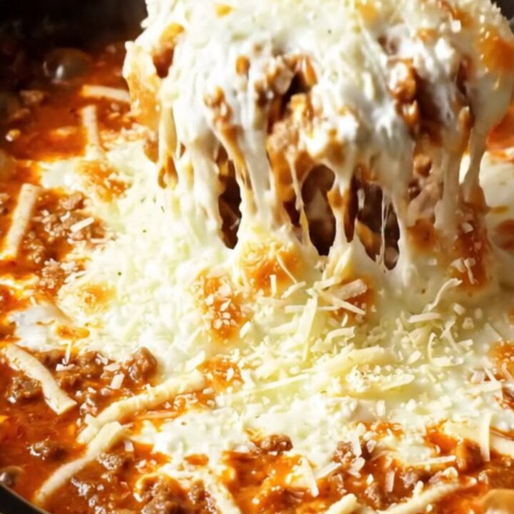A warm, bubbling lasagna dip in a deep red crockpot, with a piece of garlic bread pulling away a long string of melted