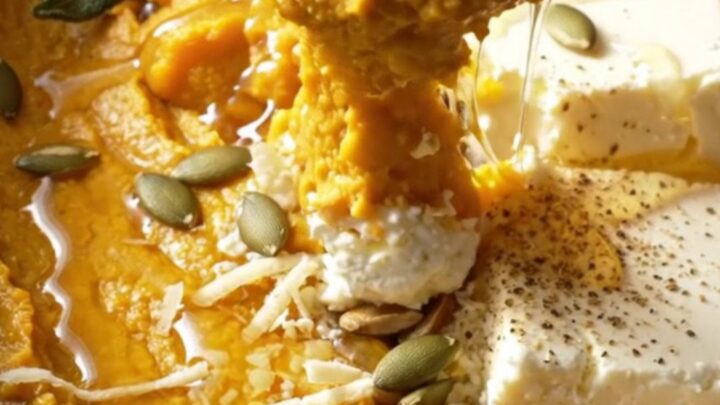 A close-up of a creamy butternut squash and goat cheese dip in a ceramic crockpot with a pita chip dipping in.