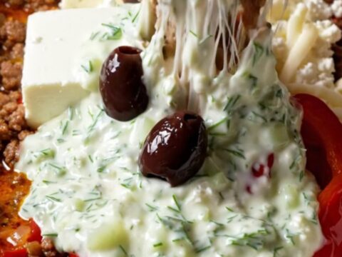 A close-up shot of a warm, bubbling Greek lamb dip in a ceramic slow cooker with a pita wedge scooping some up.