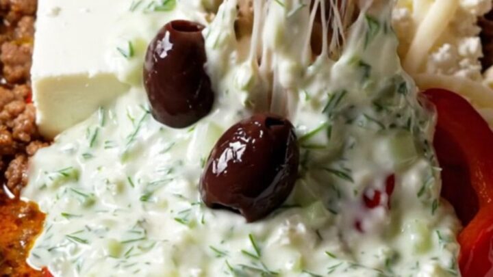 A close-up shot of a warm, bubbling Greek lamb dip in a ceramic slow cooker with a pita wedge scooping some up.