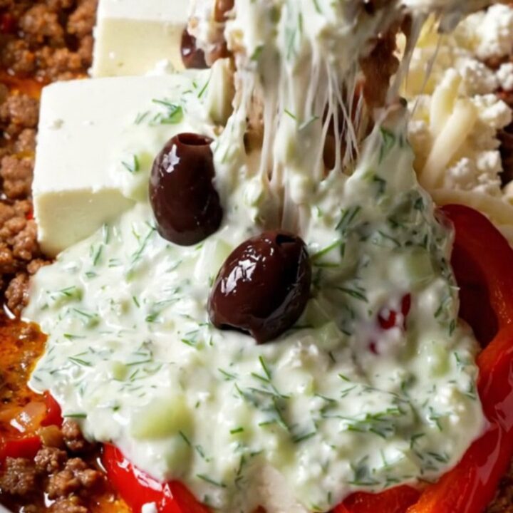 A close-up shot of a warm, bubbling Greek lamb dip in a ceramic slow cooker with a pita wedge scooping some up.
