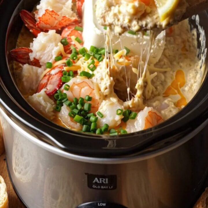 A close-up of a creamy lobster and shrimp dip in a navy blue slow cooker