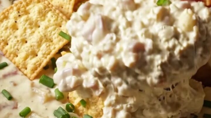 A creamy clam chowder dip in a stoneware crockpot topped with oyster crackers and chives.