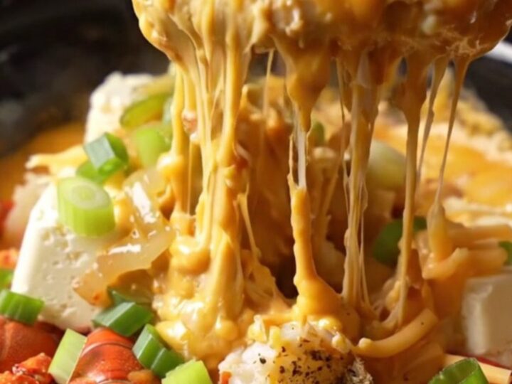 A close-up of a deep red ceramic slow cooker filled with creamy, golden-orange crawfish étouffée queso dip.