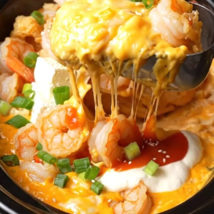 Creamy Bang Bang shrimp dip in a black ceramic slow cooker, topped with crispy shrimp, scallions, and sesame seeds.