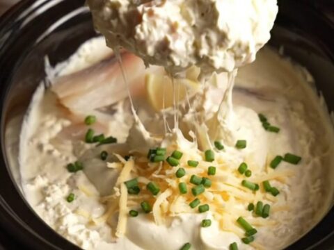 A close-up of a buttery bagel crisp being dipped into a creamy, bubbling smoked whitefish dip.