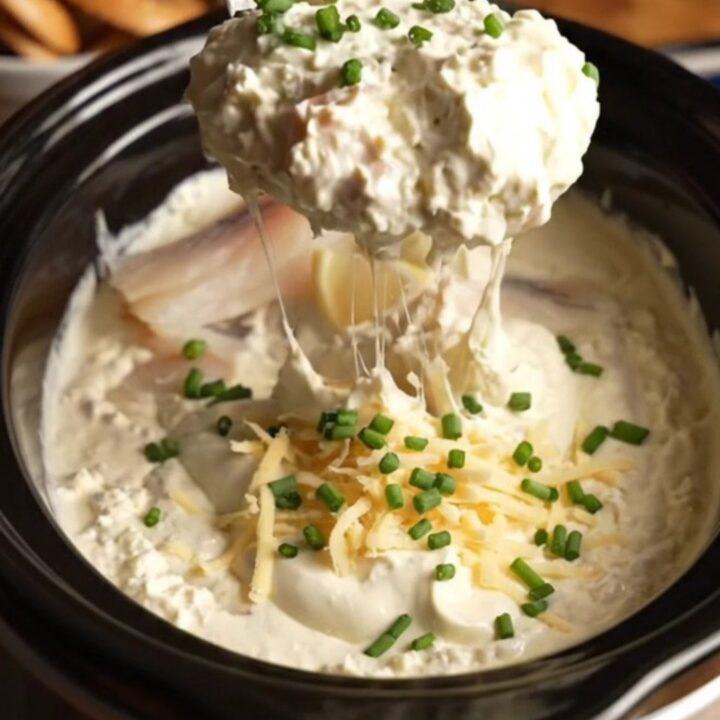 A close-up of a buttery bagel crisp being dipped into a creamy, bubbling smoked whitefish dip.