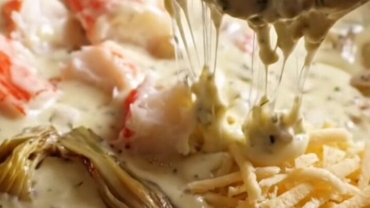 A close-up of a crispy sourdough cracker being dipped into a rich, creamy, and bubbling king crab and herb cheese dip.