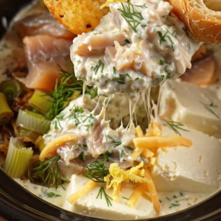 A warm cream stoneware Crockpot filled with creamy smoked trout and caramelized leek dip, garnished with fresh dill.