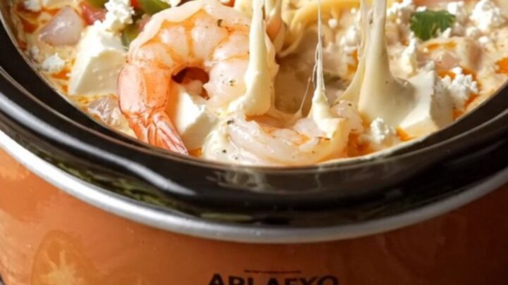 A warm ceramic crockpot filled with melted white queso, succulent shrimp, and fire-roasted chiles.