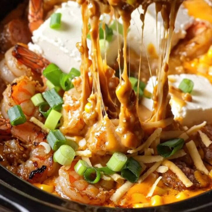 A close-up of a bubbling Crockpot filled with creamy Cajun dip featuring blackened shrimp and charred corn.