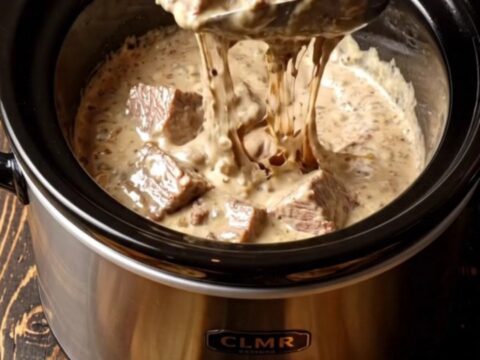A close-up of a decadent surf and turf dip in a black ceramic slow cooker, topped with chives and truffle oil.