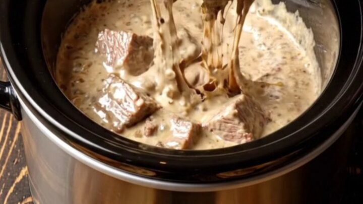 A close-up of a decadent surf and turf dip in a black ceramic slow cooker, topped with chives and truffle oil.