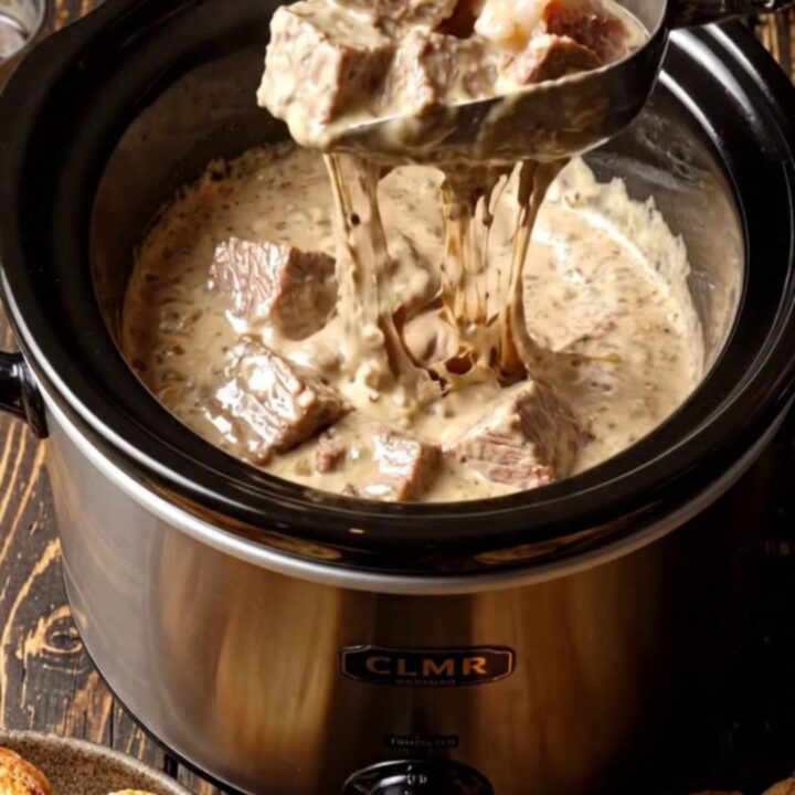 A close-up of a decadent surf and turf dip in a black ceramic slow cooker, topped with chives and truffle oil.