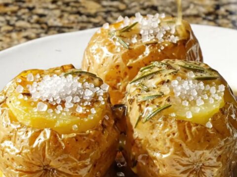 A close-up view of three perfectly cooked fondant potatoes glistening with a rich, amber herb butter glaze on a platter.