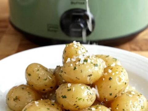 A close-up of buttery fingerling potatoes in a sage-green slow cooker, garnished with fresh dill and lemon zest.