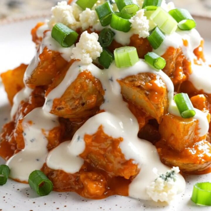 A close-up view of steaming buffalo ranch potatoes in a slow cooker, topped with melted cheese, blue cheese, and scallions.